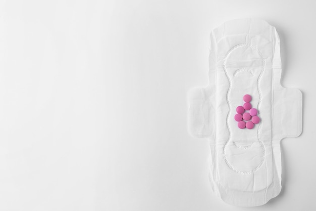 Menstrual pad and pills on white background top view with space for text Gynecological care