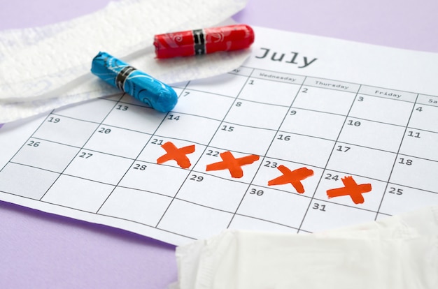 Menstrual pads and tampons on menstruation period calendar with red cross marks