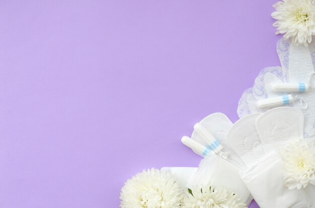 Menstrual pads and tampons with tender white flowers on pastel lilac background