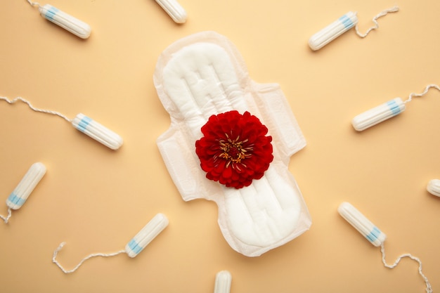 Menstrual tampons and pads on beige background. A rose flower lies on a menstrual pad. Menstruation cycle. Hygiene and protection. Top view. Vertical photo