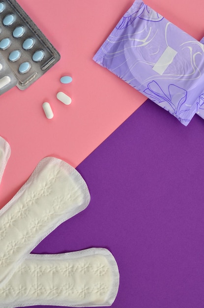 menstruatie- en dagelijkse maandverband en pillen op een roze en paarse achtergrond