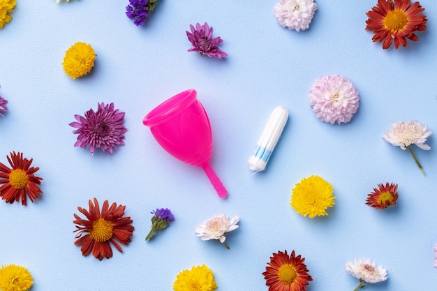 Menstruatiecup en tampons op bloemmotief achtergrond bovenaanzicht