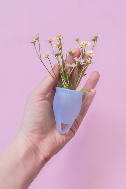 Menstruatiecup in de hand met bloemen op een roze achtergrond