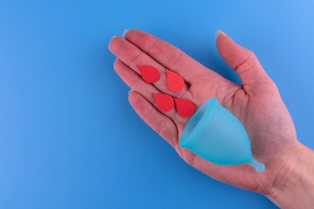 Menstruatiecup in een vrouwelijke hand op een blauwe achtergrond