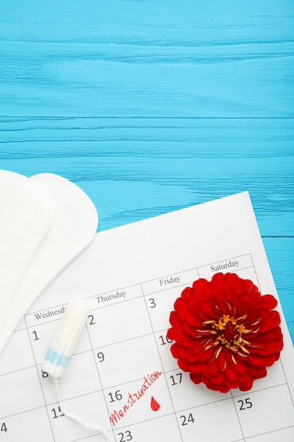 Foto calendario delle mestruazioni con tamponi di cotone e assorbenti su sfondo blu. giorni critici per la donna, protezione dell'igiene della donna. dolore mestruale