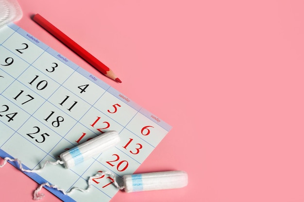 Menstruation days products calendar with red marked dates of menstruation on pink background with copy space High quality photo