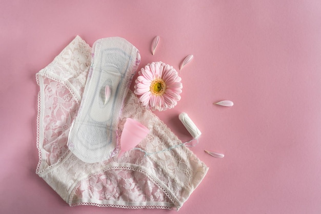Фото Концепция менструального периода гигиеническая белая женская подушка менструальная чашка и тампон с розовыми цветами