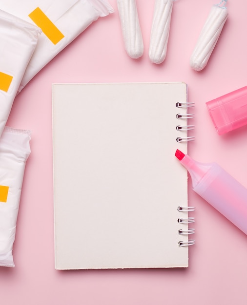 Menstruation in women. An empty notebook next to a marker, pads and tampons.