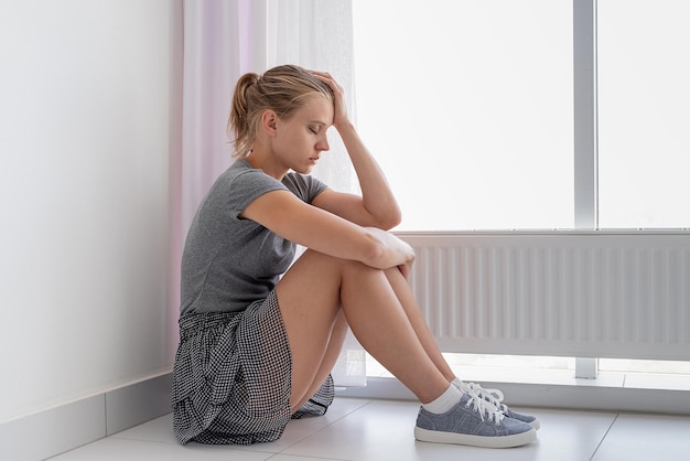 Foto salute mentale giovane donna depressa in camicia grigia e gonna seduta sul pavimento