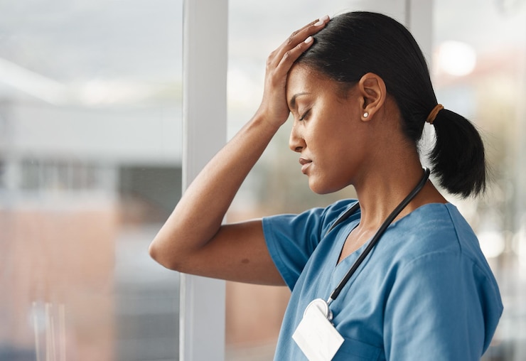 Photo mental health doctor with headache and stress standing at window at hospital burnout or overworked anxiety or depression and female nurse or caregiver holding her head for migraine pain at clinic