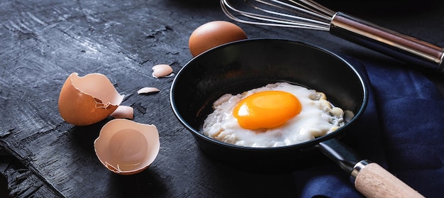 Menu koken in keuken ei gebakken ei in de pan en verse rauwe eieren op zwarte houten achtergrond