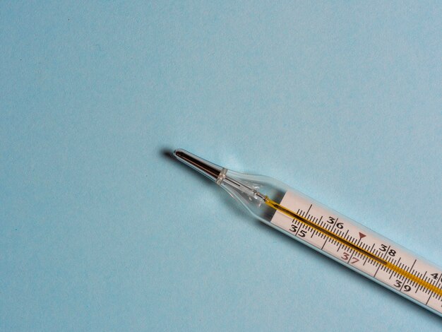 Mercury thermometer on a blue background, top view, copy space. Tool for changing the temperature of patients