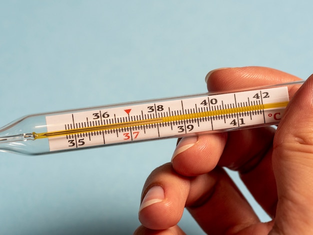 Фото Ртутный термометр на синем фоне в руке. высокая температура и болезнь