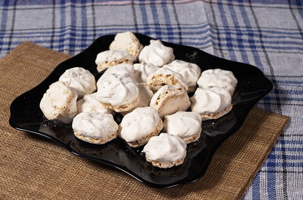 Meringue cookies with nuts in black plate on table