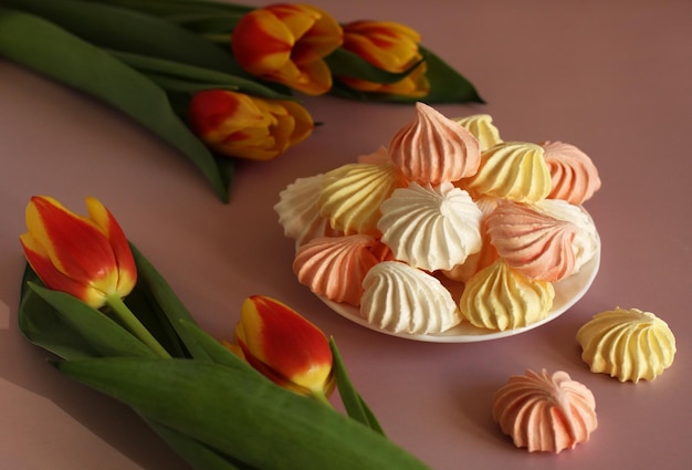 Meringue pink white yellow on a saucer on a pink background\
with variegated tulips