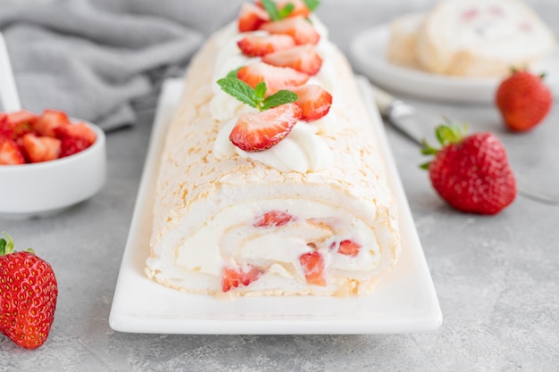 Meringue roll Pavlova cake with cream and fresh strawberries on top on a gray background Copy space