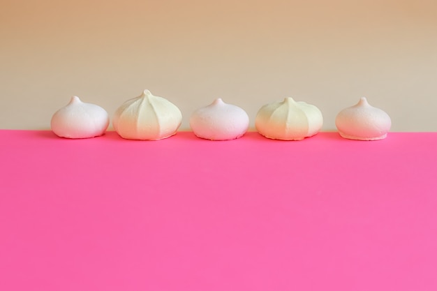 Meringue in row. Small cakes meringue on bright pink background. Delicate background with sweets.