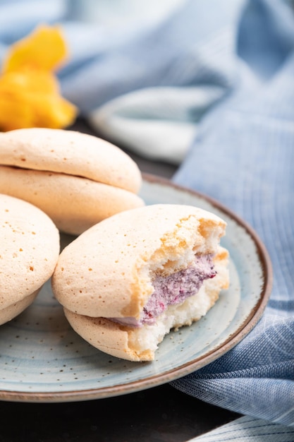 Meringues cakes with cup of coffee on a black concrete background and blue linen textile. Side view, close up, selective focus.