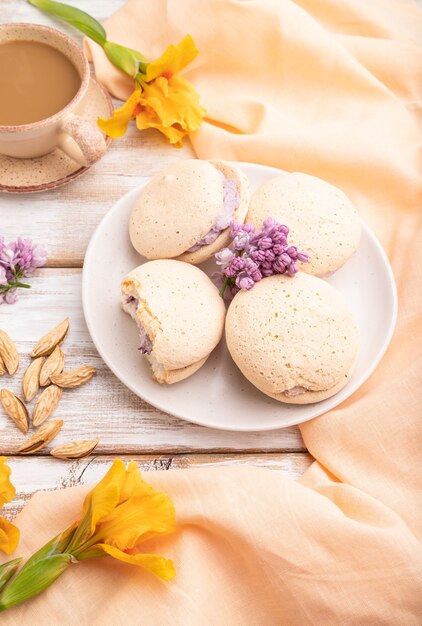 Meringues cakes with cup of coffee on a white wooden background and orange linen textile. Side view,