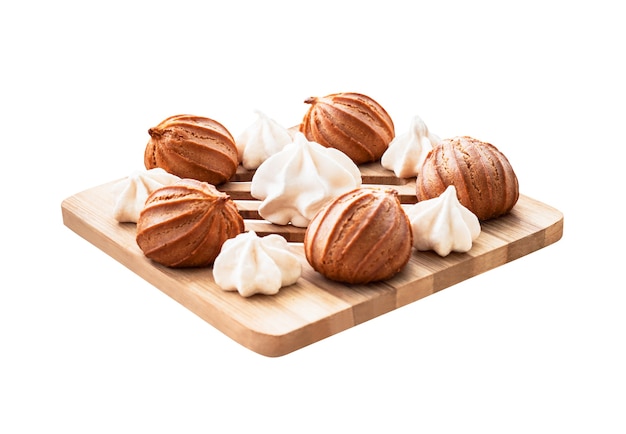 Meringues en mini-eclairs of gebakken taarten op een houten bord. Dessertvoedsel dat op witte achtergrond wordt geïsoleerd