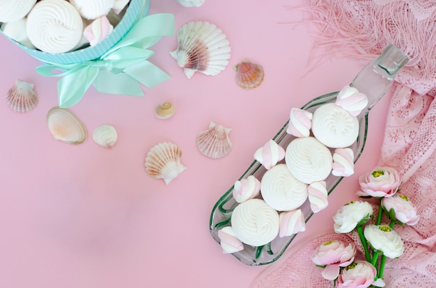 Meringues and marshmallows on handcrafted transparent serving plate on pastel pink background.