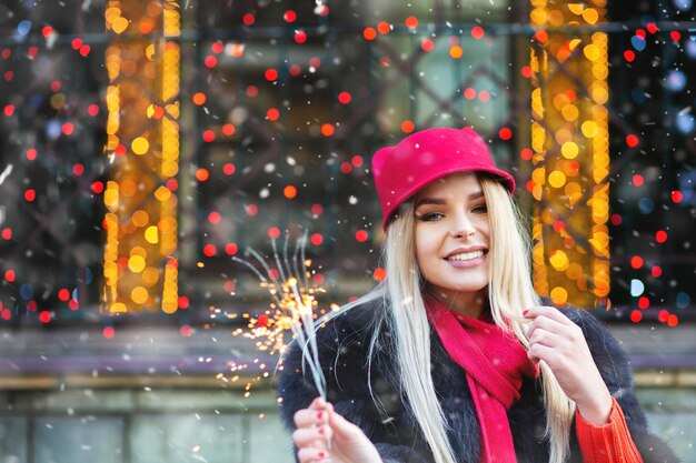 Merry blond woman having fun with sparkling lights at the Christmas fair. Space for text