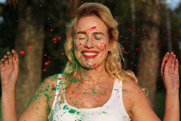 Merry blonde model wearing white shirt and posing covered with dry paint at the Holi Festival