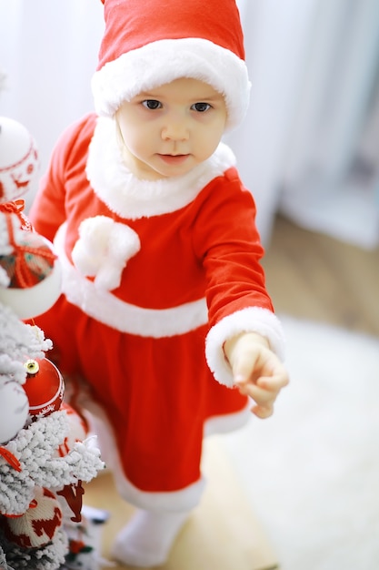 メリーブライトクリスマス。素敵な赤ちゃんはクリスマスをお楽しみください。子どものころの思い出。サンタの女の子の小さな子供は家でクリスマスを祝います。家族の休日。クリスマスツリーの近くで女の子かわいい子陽気な気分遊び。