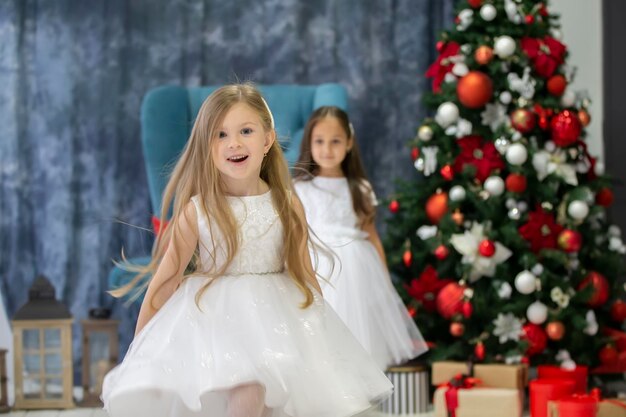 Merry children at the Christmas holiday Two little girls in elegant dresses against the background