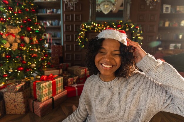 크리스마스 축하 아프리카계 미국인 여성은 클래식 어두운 인테리어에서 크리스마스 트리 근처에서 웃고 행복합니다.
