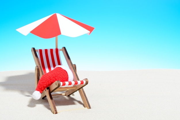 Buon natale sul concetto di spiaggia. sedia a sdraio con ombrellone e cappello di babbo natale