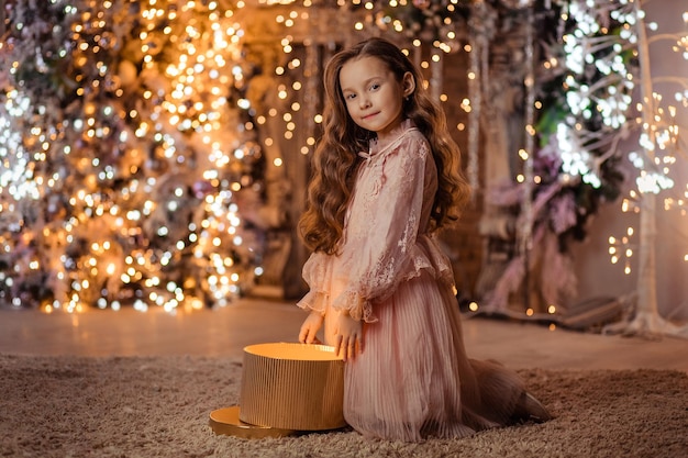 С Рождеством! Красивая девушка с волшебным подарком дома возле елки и камина