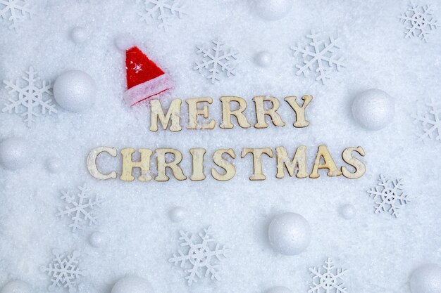 Merry christmas card, text in wooden letters on white snow, snowflakes, christmas hat