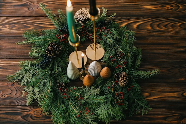 Merry Christmas Christmas trees and candles in rustic christmas wreath on dark wood Festive modern decor Miniature pine trees candlestick and modern wreath with berries and pine cones