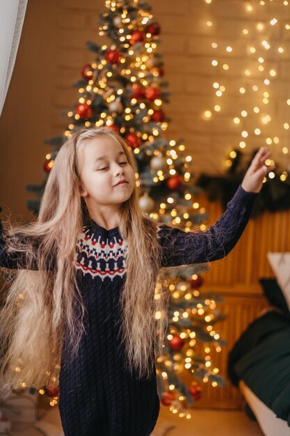 메리 크리스마스 개념입니다. 아이는 집에 있는 크리스마스 트리 근처에서 즐겁게 춤을 추고 있습니다. 집에서 메리 크리스마스 축 하입니다.