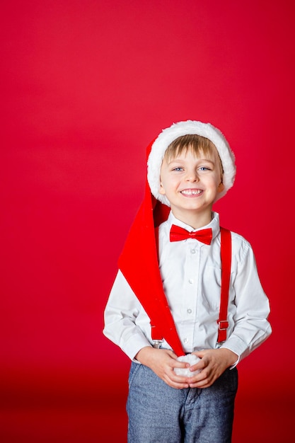 Merry Christmas Cute cheerful little boy in Santa Claus hat on red background happy childhood