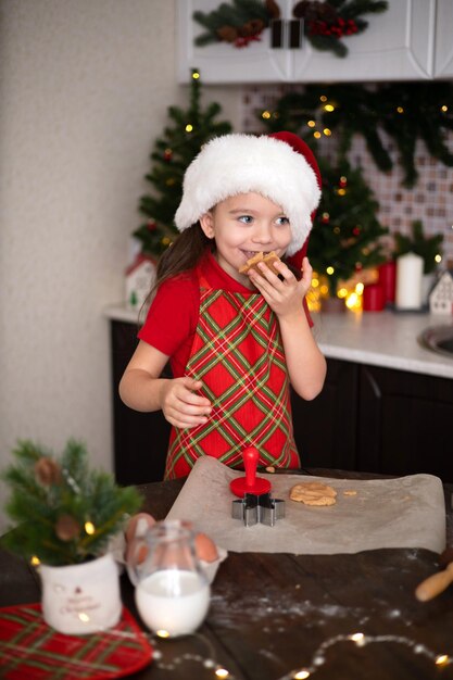 Merry Christmas Cute girl child makes Christmas cookies in her decorated kitchen Lights and a Christmas tree Lifestyle Space for text