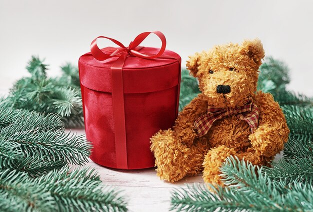 Merry Christmas gift box and soft toy bear greeting card. Gifts, fir tree branches. Red Luxury New Year present. Christmastime celebration.