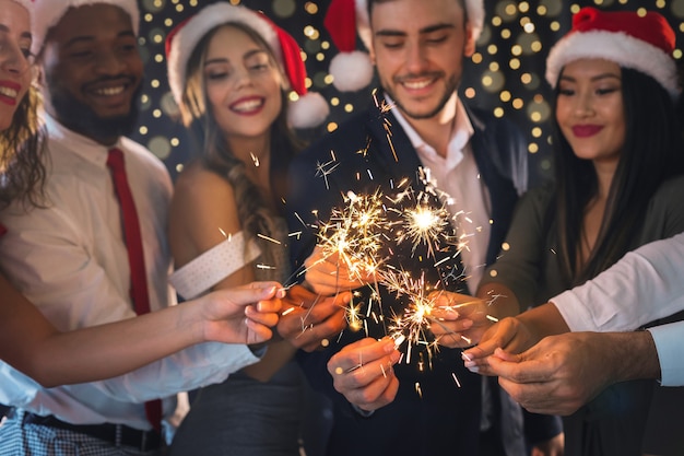 Photo merry christmas greeting card. group of happy friends in new year eve with sparkling bengal lights, closeup