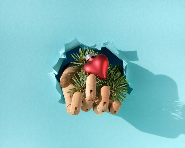 Merry christmas hand with fir twigs and heart shaped red xmas toy through paper hole