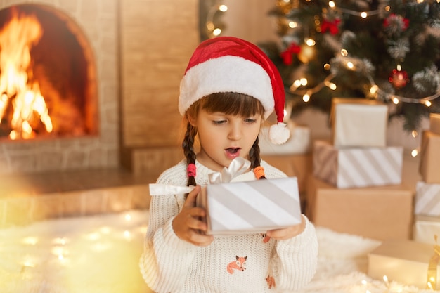 С Рождеством! Счастливый ребенок с подарочной коробкой дома в украшенной гостиной
