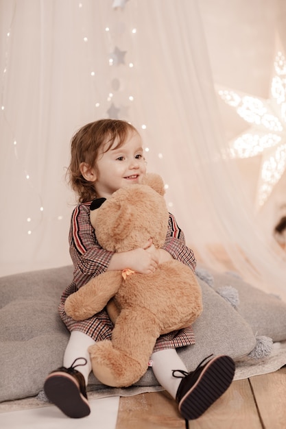 写真 メリークリスマス。自宅でドレスを着たテディベアと幸せなかわいい巻き毛の少女。