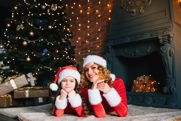 Buon natale e buone feste! la bella madre con la piccola figlia in costumi di natale trascorre del tempo insieme vicino all'albero di natale.