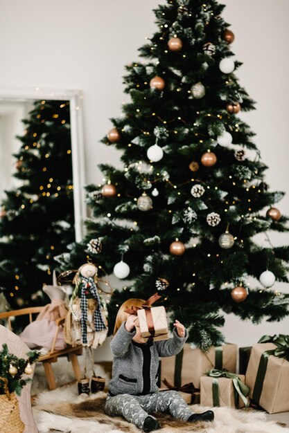 Merry Christmas and Happy Holidays Cheerful cute child girl opening gifts Kid having fun near tree in the morning Loving family with presents in room