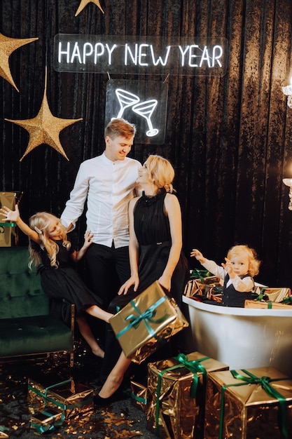 Photo merry christmas and happy holidays cheerful and happy family with christmas presents in golden wrappings and dark background children are having fun loving family with gifts in the room