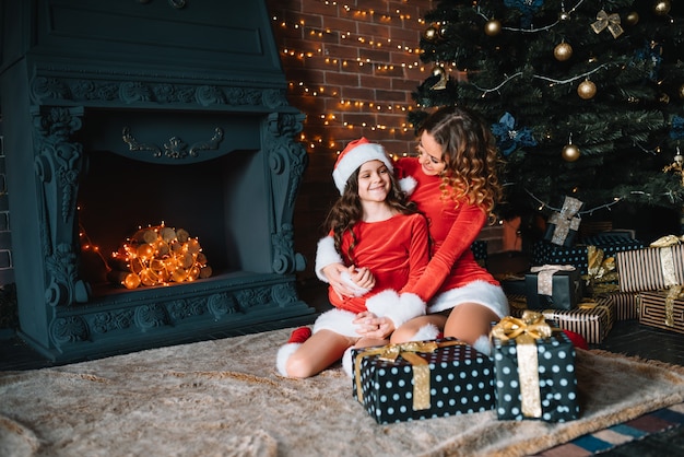 メリークリスマスとハッピーホリデー！陽気なお母さんとクリスマスの衣装を着たかわいい娘の女の子がプレゼントを交換します。