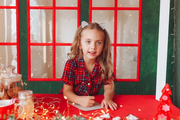 Merry christmas and happy holidays a cute little girl in\
pajamas writes a letter to santa claus near the christmas tree\
indoors children