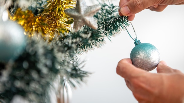 メリークリスマスと幸せな休日、男の手が冬に家の屋内でトウヒの木を飾っています。クリスマスボールと装飾バナー、新年のコンセプトのためのモミの枝の見掛け倒しの吊り下げ。