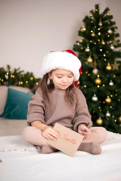 Merry Christmas and Happy Holidays The little happy girl on the bed wrote a letter to Santa Claus and holds the envelope in her hand