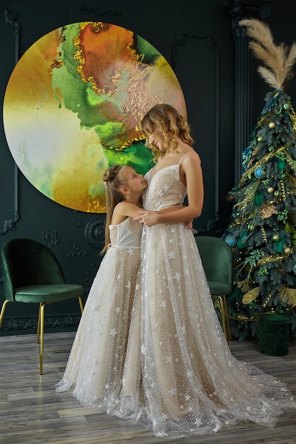 メリークリスマスとハッピーホリデー。ママと娘は屋内でクリスマスツリーを飾ります。同じドレスを着た母と娘。肖像画を愛する家族のクローズアップ。